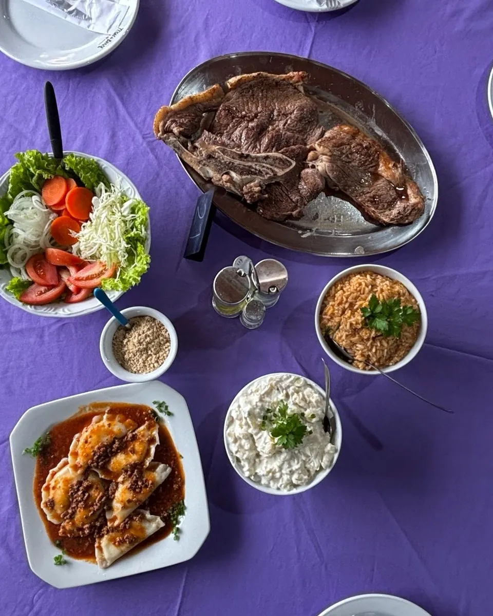 Mesa com toalha lilás servida com churrasco, saladas e acompanhamentos